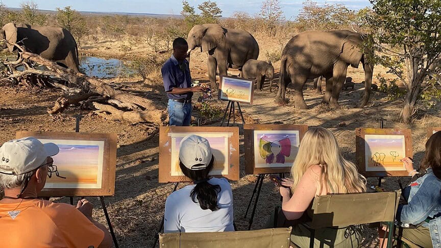 Painting elephants on easels with elephants in the background