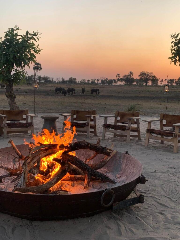Firepit at Qorokwe Camp in Botswana at sunset with elephants standing in the background