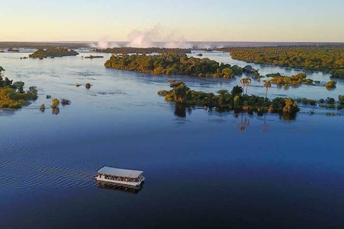 Spray from Victoria Falls can be seen from a distance when you are on a sunset cruise on the Zambezi River in Victoria Falls