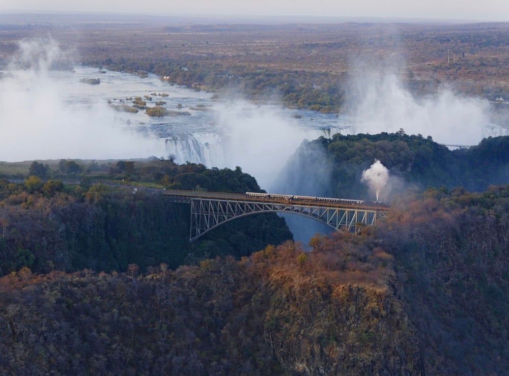 Bushtracks Express steam train crossing over the Victoria Falls Bridge with the Victoria Falls in the background.
