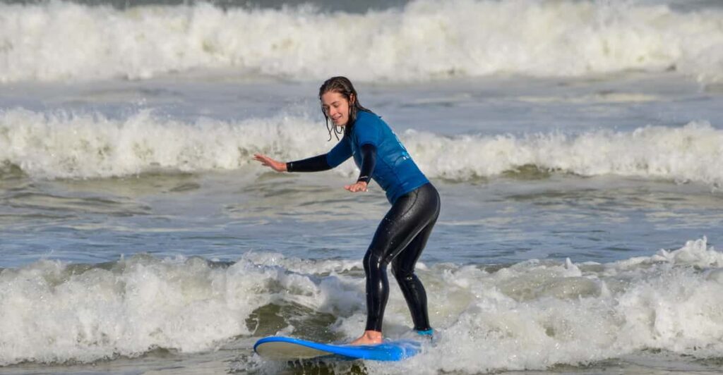 Woman standing on a surfboard  at Muizenberg beach as she is having a surfing lesson which is a popular watersport in Cape Town