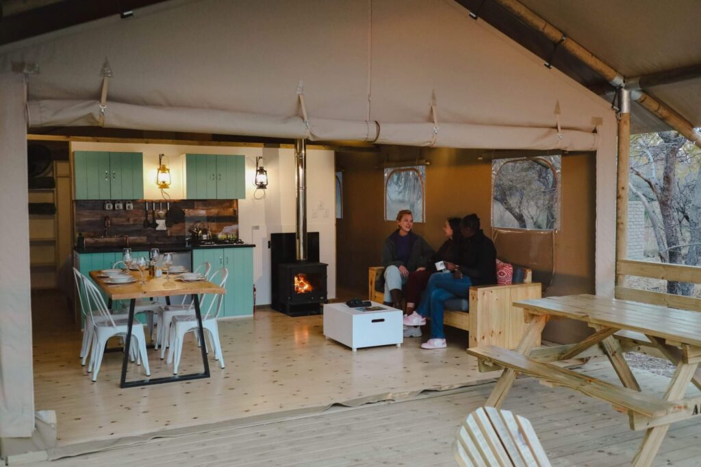 Africamps tent interior showing the kitchen, dining room and lounge area wiht a woodfired fireplace.