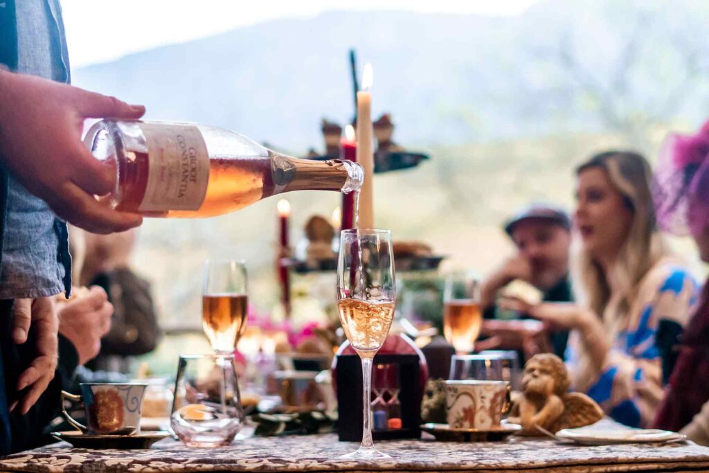 People sitting around a table enjoying lunch and someone is pouring sparkling wine from Groot Constantia into a champagne glass.