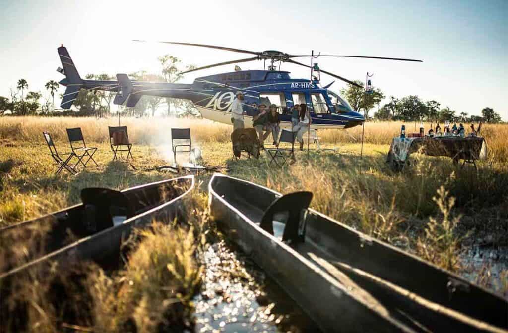 Scenic helicopter flight on the ground in Botswana next to a table of drinks and mokoros ready to take travellers into the cool Delta waters