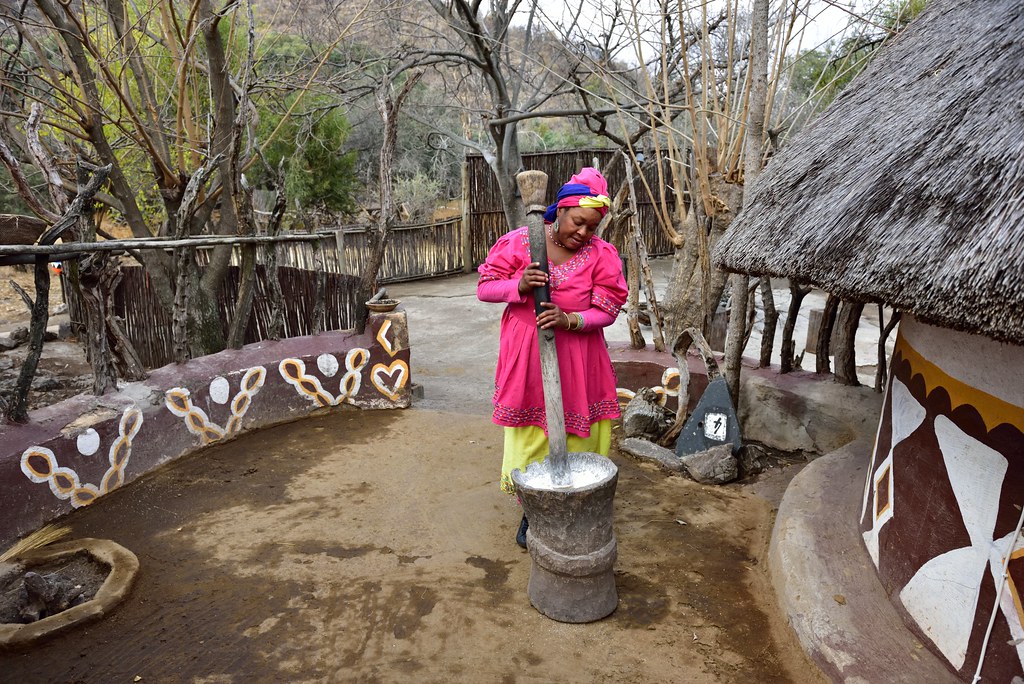 A woman in the Lesedi Cultural Village grinding grain with a large mortar and pestle.