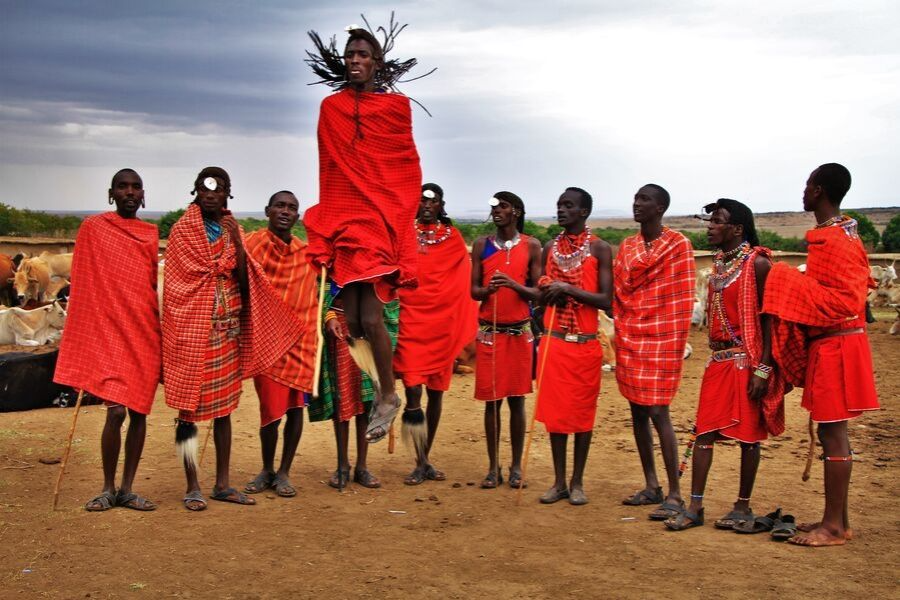 Maasai people in Kenya wearing traditional red blankets. One man is jumping.